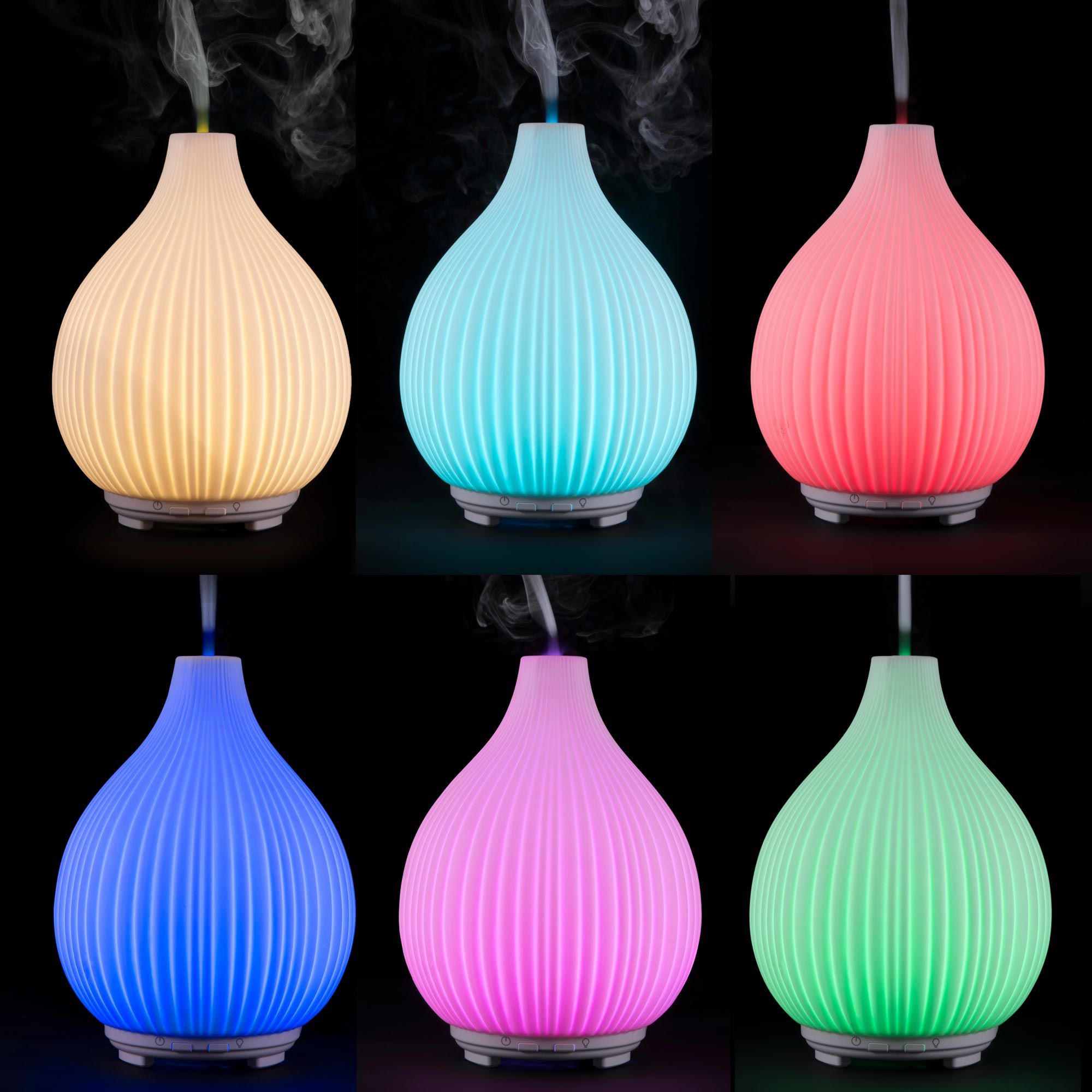 Six LYLA Aroma Diffuser, Humidifier & Night-Lights by Rio glow in yellow, teal, pink (top), and blue, purple, green (bottom), emitting vapor in multicolored hues to create a calming ambiance against a black background.